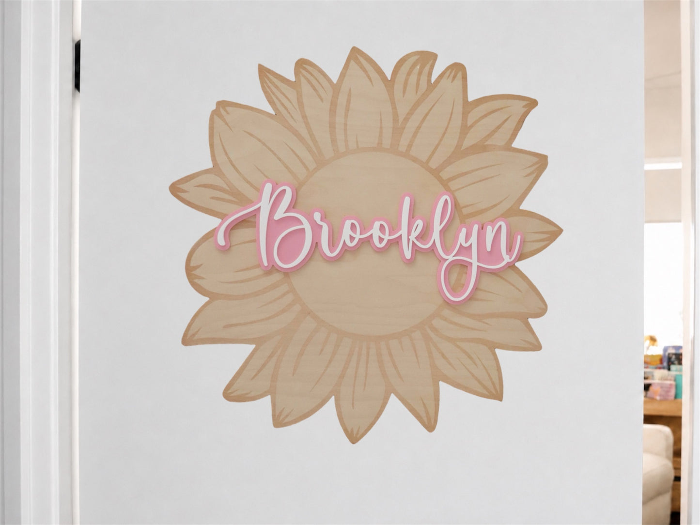 A personalized sunflower wall decal with the name 'Brooklyn' in pink script, displayed on a white door in an indoor room setting.